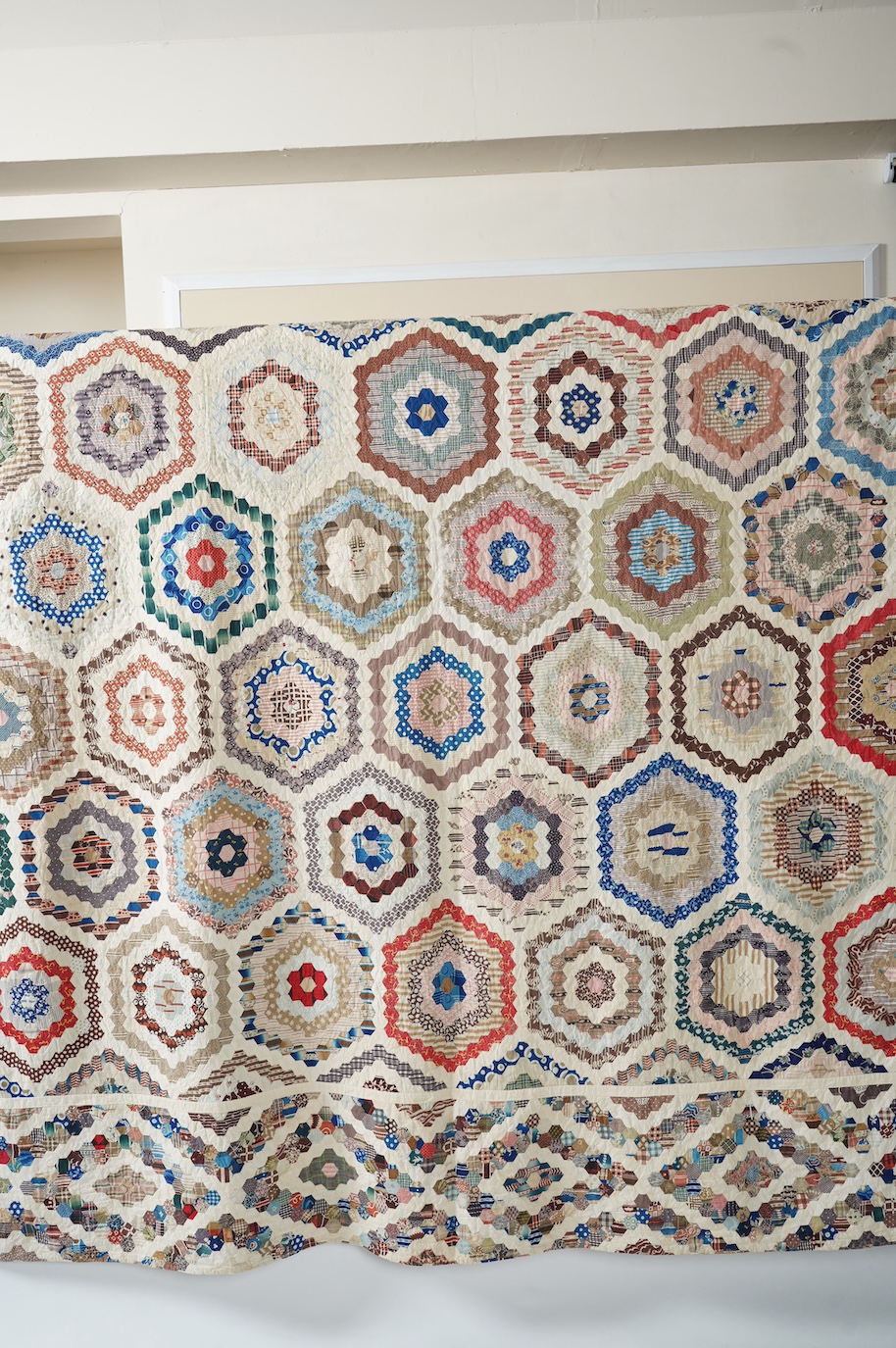 A large 19th century ‘Grandmother’s Flower Garden’ cotton patchwork bedspread, using dress fabric scraps from the day to create hexagonal concentric patterns which form a flower like shape/pattern, 282 x 254cm. Condition